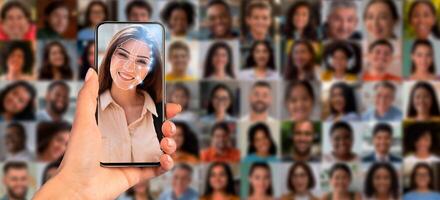 A hand holds a smartphone displaying facial recognition technology, highlighting a person's face against a collage of diverse portraits, showcasing modern identification methods and technology. photo