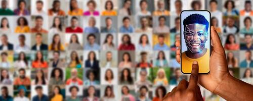 A hand holds a smartphone displaying a face scan of a smiling individual. Behind are numerous portraits of different people, emphasizing modern identification technology. photo