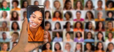 In a bright setting, a person holds a smartphone displaying a smiling face among a collage of diverse portraits, highlighting advances in recognition technology. photo