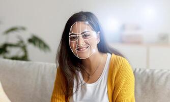 Indian woman sits on a couch with a smiling expression as facial recognition technology analyzes her features in a home setting. This reflects a shift towards digital identification in daily activities. photo