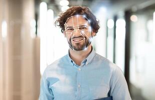A man stands in a bright, contemporary hallway while his facial features are captured by advanced recognition technology. photo