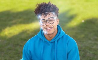 A person with glasses smiles while facial recognition technology analyzes their features outdoors in a sunny environment. This reflects the integration of modern tech into daily life. photo