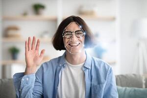 A person with a joyful expression waves while experiencing facial recognition technology at home. This showcases the integration of modern tech in everyday life, emphasizing personal interaction. photo