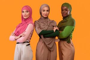 Three Gorgeous Diverse Muslim Ladies In Hijab Posing Crossing Hands Smiling To Camera Standing Together On Yellow Studio Background. Arabic Female Beauty And Fashion Concept photo