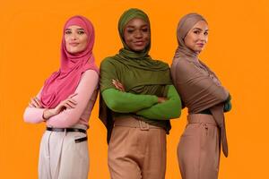 Three Successful Modern Muslim Women In Hijab Crossing Hands Smiling To Camera Standing Over Yellow Studio Background. Arabic Ladies Posing In Headscarf. Islamic Females Diversity Concept photo