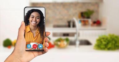 A person is enjoying a call on a smartphone while sitting in a cozy kitchen. Recipient smiling and engaged. Telecommunication concept photo