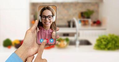 A person at home uses a smartphone to connect with a friend via call. The vibrant kitchen background adds a lively touch to the telecommunication experience. photo