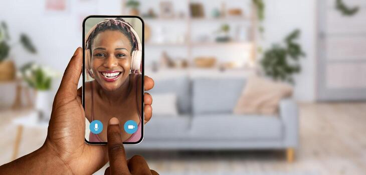 A person engaged in a call using a smartphone shows a smiling face on the screen. Bright decor and a comfortable couch create a warm home atmosphere, enhancing connectivity. photo