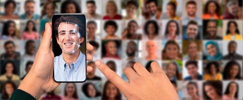 A person's hand holds a smartphone displaying a facial recognition scan of a smiling face. The background is a collage of diverse faces, showcasing modern technology in identification. photo