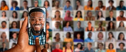 A person uses a smartphone for face recognition, showcasing advanced technology. Behind are diverse portraits of people, illustrating the depth of modern identification methods. photo