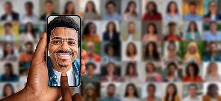 A hand holds a smartphone displaying a face recognition scan of a smiling man. Behind are various blurred portraits of people, illustrating advanced identification technology in action. photo
