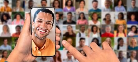 A hand holds a smartphone displaying a face recognition interface. Multiple portraits of people can be seen in the background, illustrating modern identification technology at work. photo
