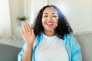 A person with curly hair smiles while waving, engaging in a facial recognition identification process. The modern setting reflects the integration of technology into everyday life. photo