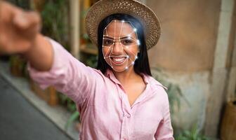 A person is engaging with innovative facial recognition technology outdoors. The individual is smiling while showcasing a digital overlay highlighting facial features in a vibrant urban setting. photo