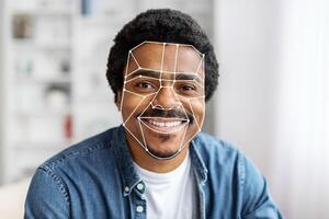 African American man is using facial recognition technology for identification at home. The digital overlay emphasizes facial features, showcasing advanced tech for seamless verification. photo