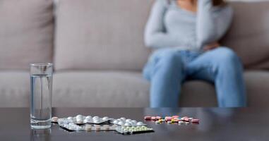 Suicide by medication overdose concept. Heap of pills and glass of water on table and blurred young woman with depression crying on background, copy space. Selective focus photo