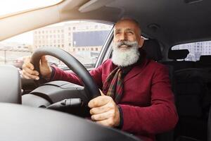 Handsome elderly grey-haired man with long beard sitting inside new car, traveling alone or going to office, senior businessman going to business meeting by his auto, shot from front panel photo