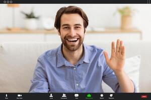 Hello. Happy Man Waving Hand Smiling To Camera Sitting On Couch At Home. Cheerful Guy Gesturing Hi Greeting Making Call Indoors. Modern Remote Communication Concept photo