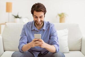 Excited Man Using Phone Networking Texting On Cellphone And Browsing Internet Sitting On Sofa At Home. New Mobile Application For Smartphone Concept. Selective Focus photo