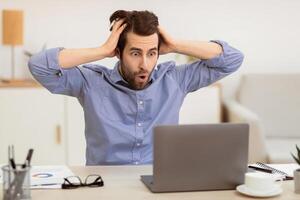 Oops, Computer Problem. Shocked Frustrated Businessman Looking At Laptop Screen Touching Head Having Issue At Workplace Working Online At Home Office. Internet Connection Problems Concept photo
