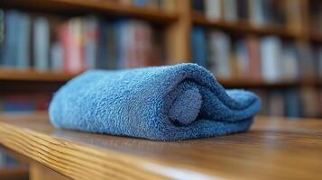 A crisp, soft blue towel rests on a smooth wooden table surrounded by bookshelves. photo