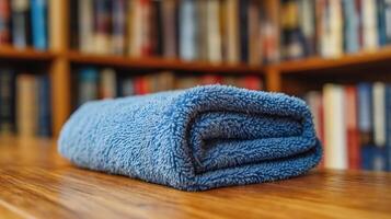 A neatly folded blue towel placed on a wooden table surrounded by bookshelves full of books. photo