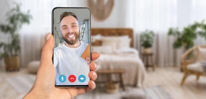 A person holding a smartphone displaying a call. The cozy home setting is decorated with plants, and natural light fills the room, creating an inviting atmosphere. photo