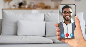 A person enjoys a lively call from their living room, holding a smartphone with a smiling individual on the screen. The cozy setting enhances the communication experience. photo
