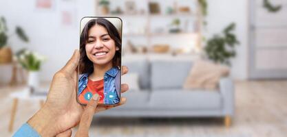 A person is having a friendly call on a smartphone, enjoying the conversation with smiling Arab woman. The cozy home environment features a sofa and decorative elements in the background. photo