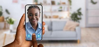 A person is participating in a call using a smartphone, woman on screen showing a joyful smile. The background features a cozy living room, enhancing the homey atmosphere. photo