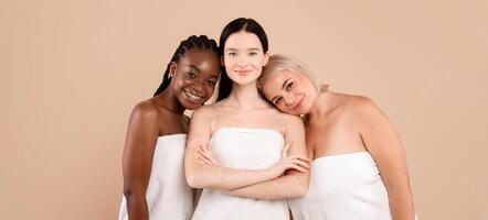 Happy Multi-Ethnic Women With Different Skin And Body Types Wearing Bath Towels Standing Over Beige Studio Background, Attractive Young Interracial Females Posing After Spa Treatments, Copy Space photo