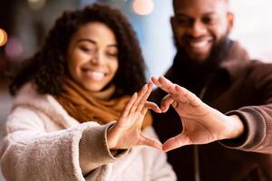 Romantic Relationship Concept. Portrait of happy smiling black african american couple making heart shape with hands walking together in the evening, selective focus. Love, Connection And Bonding photo