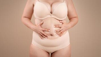 Obesity And Overweight. Cropped Portrait Of Plus Size Woman In Underwear Standing Over Beige Studio Background, Unrecognizable Curvy Lady In Lingerie Touching Belly, Suffering From Body Shaming photo
