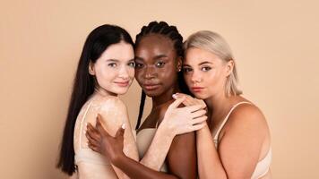 Group Of Three Multiracial Woman With Different Body And Skin Types Posing Together Over Beige Studio Background. Beautiful Ladies In Underwear Embracing And Looking At Camera, Closeup Portrait photo