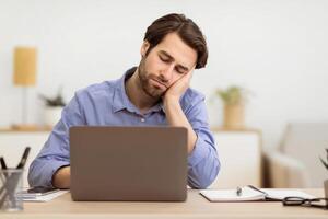 Tired Businessman Sleeping At Laptop Computer Sitting At Desk At Workplace In Modern Office. Insomnia And Fatigue Problem, Boring Job Concept. Selective Focus photo