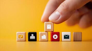 A hand placing a wooden block with an envelope icon among other blocks on a vibrant yellow background photo