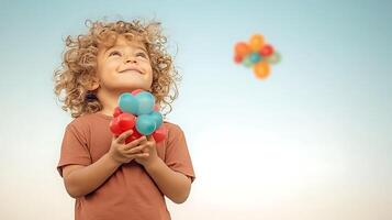 A joyful child with curly hair holding colorful balloons against a clear sky, smiling happily photo