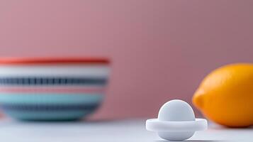 A minimalist composition featuring a white pacifier, a lemon, and a striped bowl against a pink background photo