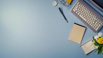 A serene workspace featuring a keyboard, notepad, and flowers on a blue background photo