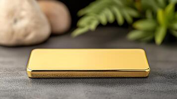 A shiny gold bar resting on a textured surface surrounded by soft greenery and a plush toy photo
