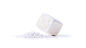 A single white sugar cube leaning on a pile of granulated sugar against a clean background photo