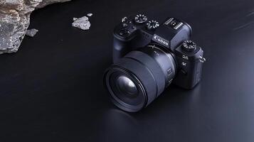 A sleek camera positioned on a dark surface, showcasing its lens and controls, with rocks nearby photo