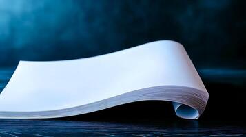 A smooth, blank sheet of paper elegantly curves on a dark surface with a soft blue background photo