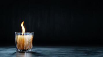 A solitary candle flickers in a dark setting, casting warm light and shadows around photo