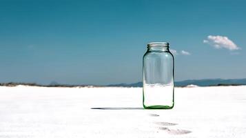 A solitary glass jar stands on a pristine white sandy beach under a clear blue sky photo