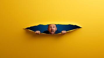 A surprised man peeking through a torn yellow paper, with a blue background enhancing the effect photo