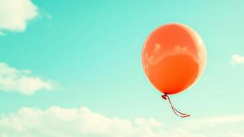 A vibrant orange balloon floats against a clear blue sky with soft clouds in the background photo