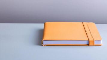 A vibrant orange notebook resting on a minimalist blue table against a soft gradient background photo