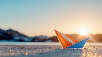 A vibrant paper boat rests on a serene beach at sunset, with mountains softly illuminated in the background photo