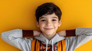 Cheerful boy with backpack posing against a bright yellow background, smiling happily photo